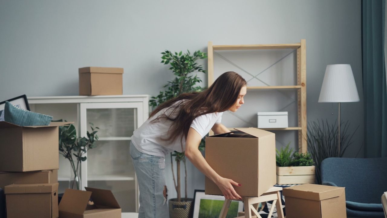 A young woman with long hair arranging boxes in her new home. Ideal for moving and lifestyle stories.